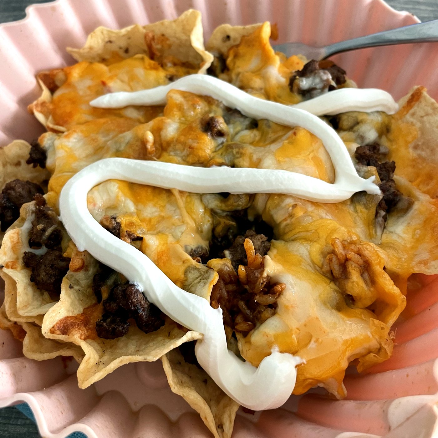 Air fryer nachos with melted cheese, taco meat and a zigzag of sour cream